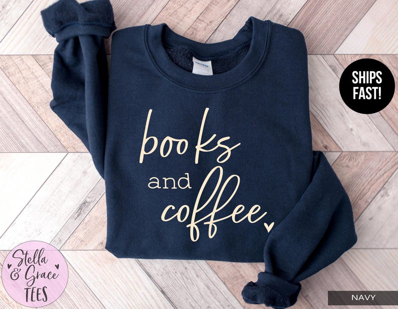 May include: Navy blue sweatshirt with the words "books and coffee" in a cursive font. The sweatshirt has a crew neck and long sleeves. The text is in a light beige color. The brand name "Stella & Grace Tees" is in a pink circle.