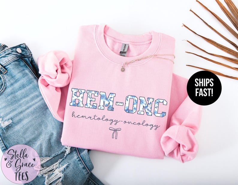 May include: Pink sweatshirt with the text "HEM-ONC hematology-oncology" in blue and white lettering with a small bow.