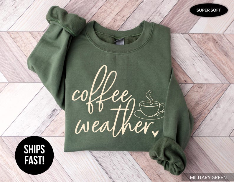 May include: Military green sweatshirt with the words "coffee weather" in a cursive font, along with a coffee cup graphic. The sweatshirt is made of a soft material. The text "SUPER SOFT" is in the upper right corner.