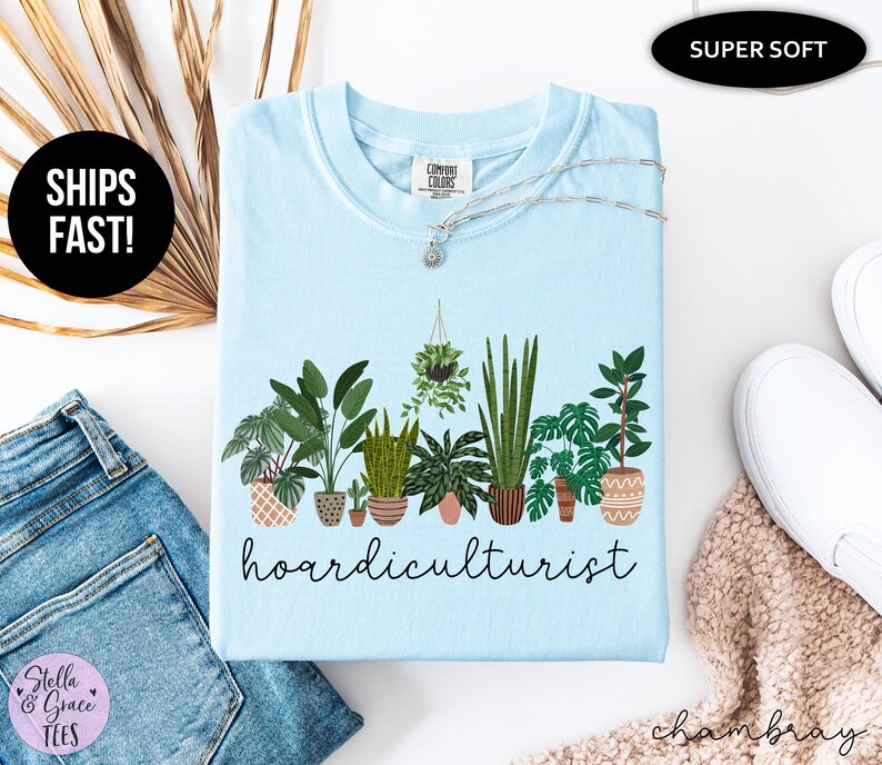 Op de afbeelding: Lichtblauw T-shirt met een afbeelding van diverse potplanten en het woord "hoardiculturist" in zwart schrift. Een zilveren ketting met een kleine hanger ligt op het shirt. Het shirt is voorzien van de labels "Super Soft" en "Comfort Colors".