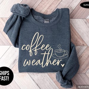 May include: Heather dark grey sweatshirt with the words "coffee weather" in a cream-colored script, along with a coffee cup graphic. The sweatshirt is super soft and has rolled-up sleeves.