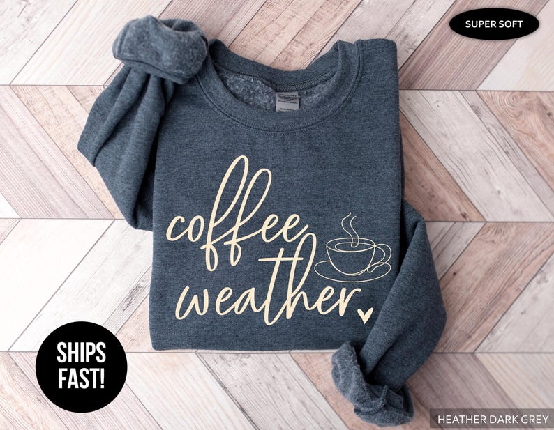 May include: Heather dark grey sweatshirt with the words "coffee weather" in a cream-colored script, along with a coffee cup graphic. The sweatshirt is super soft and has rolled-up sleeves.