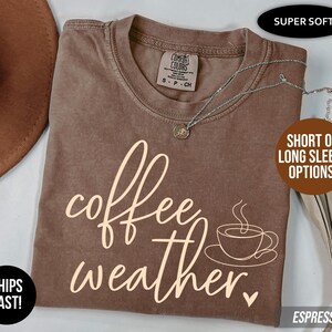 May include: Espresso-colored t-shirt with the words "coffee weather" in a cursive font, along with a coffee cup graphic. The shirt has a crew neck and short sleeves. The shirt is labeled "Super Soft" and has "Short or Long Sleeve Options!"