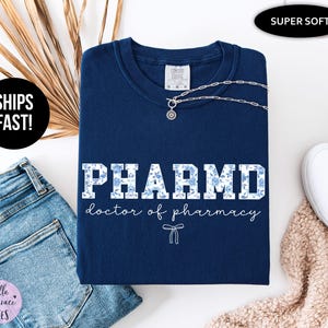 Puede incluir: Camiseta azul marino con un dise&ntilde;o de estampado floral blanco que dice "PHARMD doctor of pharmacy".