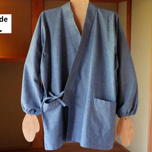 以下が含まれることがあります： 伸縮性のある袖口を備えた長袖、Vネック、サイドタイ留め、2つのフロントパッチポケットが特徴の青いシャンブレーラップジャケット。画像左上に「Wide L」というテキストが表示されています。