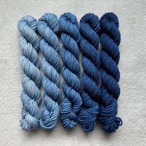 Op de afbeelding: Zes bollen garen in tinten blauw, variërend van licht tot donker. Het garen is gerangschikt in een verloop van licht naar donker.