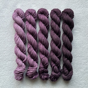 Könnte beinhalten: Sechs Knäuel handgefärbter Wolle in Violetttönen, von helllila bis tief dunkelblau.