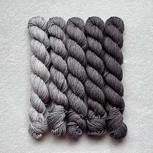 May include: Six skeins of yarn in shades of gray, from light to dark, arranged in a gradient.