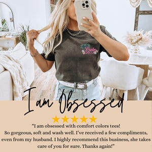 K&ouml;nnte beinhalten: Eine Frau tr&auml;gt ein dunkelgraues T-Shirt mit dem Text "Psalm 35" und einem Blumendesign. Das T-Shirt ist weich und bequem. Die Frau l&auml;chelt und h&auml;lt ein Telefon in der Hand. Der Text "Ich bin besessen" ist in gro&szlig;en Buchstaben unter dem Bild geschrieben. F&uuml;nf Sterne sind unter dem Text angezeigt. Der Text "Ich bin besessen von bequemen T-Shirts in verschiedenen Farben! So wundersch&ouml;n, weich und waschbar. Ich habe ein paar Komplimente bekommen, sogar von meinem Mann. Ich kann dieses Gesch&auml;ft nur w&auml;rmstens empfehlen, sie k&uuml;mmert sich wirklich um dich. Danke nochmal!" ist unter den Sternen geschrieben.