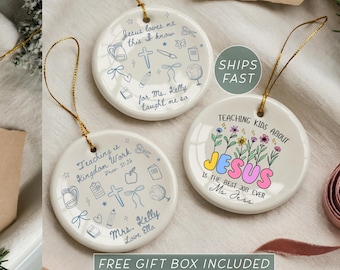 May include: Three round white ceramic ornaments with gold hanging strings. Two ornaments feature blue line art of school supplies, a cross, and text including Jesus loves me this I know and Teaching is Kingdom Work. One features colorful flowers and text.