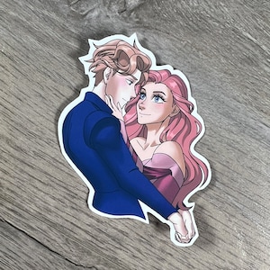 Puede incluir: Una pegatina con una ilustración romántica de una pareja abrazándose. El hombre tiene el pelo castaño y lleva un traje azul. La mujer tiene el pelo largo y rosa y lleva un vestido rosa.