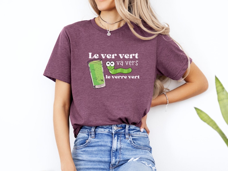 Puede incluir: Una camiseta morada con un gusano verde y un vaso de l&iacute;quido verde. El texto en la camiseta dice "Le ver vert va vers le verre vert".