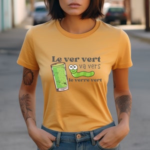Puede incluir: Una camiseta amarilla con un gusano verde y un vaso de l&iacute;quido verde. El texto en la camiseta dice "Le ver vert va vers le verre vert".