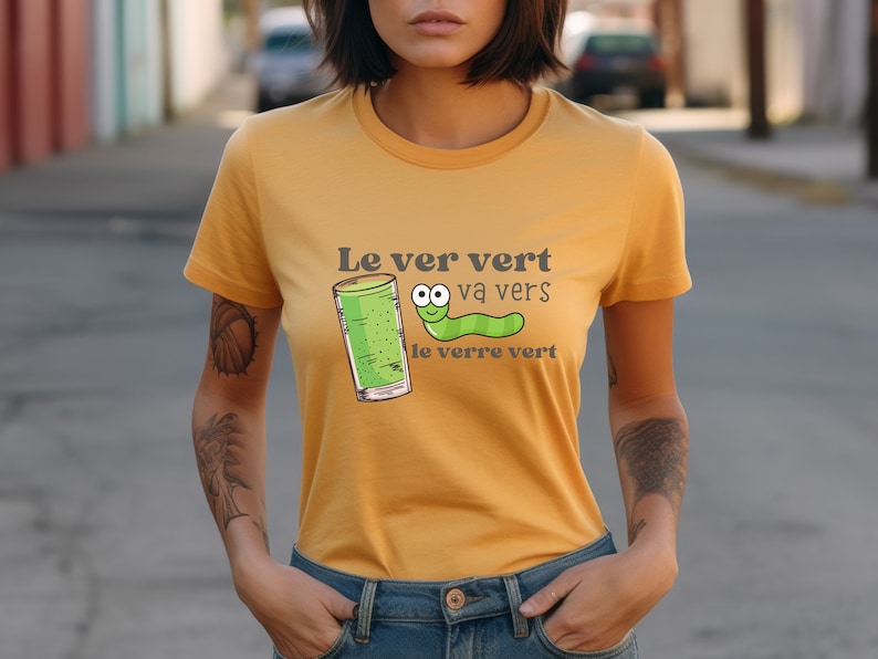 Puede incluir: Una camiseta amarilla con un gusano verde y un vaso de l&iacute;quido verde. El texto en la camiseta dice "Le ver vert va vers le verre vert".