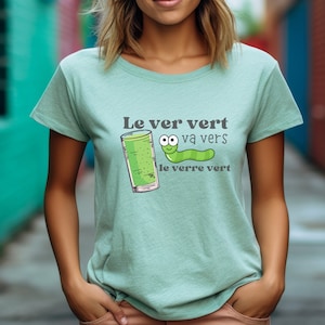 May include: A light green t-shirt with a cartoon worm and a glass of green liquid. The text on the shirt reads "Le ver vert va vers le verre vert".