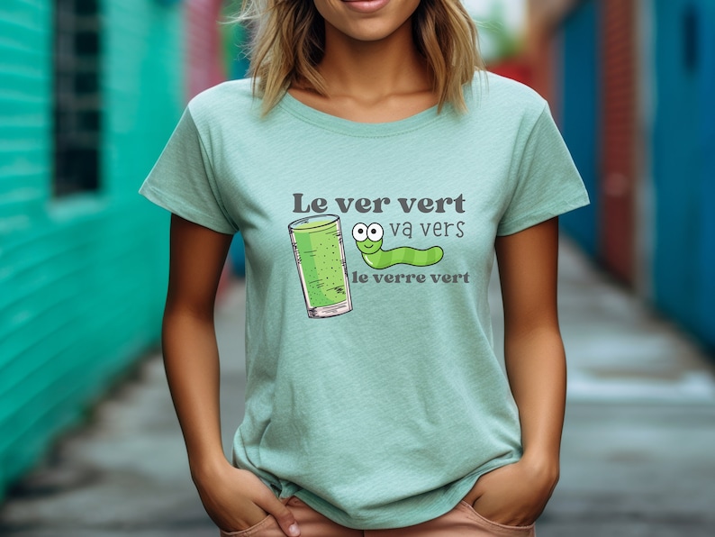 Puede incluir: Una camiseta verde claro con un gusano de dibujos animados y un vaso de l&iacute;quido verde. El texto en la camiseta dice "Le ver vert va vers le verre vert".