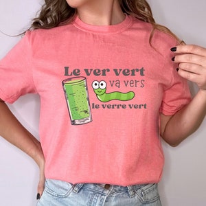 Puede incluir: Una camiseta rosa con un gusano verde y un vaso de l&iacute;quido verde. El texto en la camiseta dice "Le ver vert va vers le verre vert".