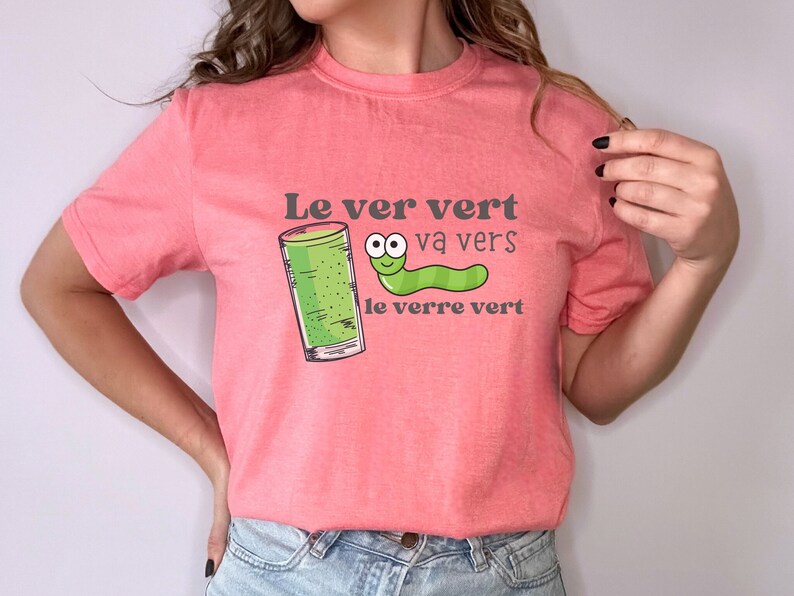 Puede incluir: Una camiseta rosa con un gusano verde y un vaso de l&iacute;quido verde. El texto en la camiseta dice "Le ver vert va vers le verre vert".