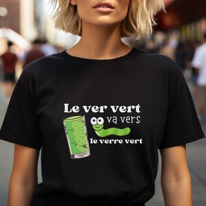 Puede incluir: Una camiseta negra con un gr&aacute;fico blanco de un gusano verde con ojos saltones y el texto "Le ver vert va vers le verre vert".
