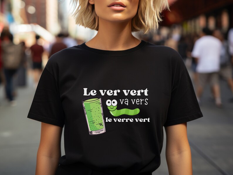 Puede incluir: Una camiseta negra con un gr&aacute;fico blanco de un gusano verde con ojos saltones y el texto "Le ver vert va vers le verre vert".