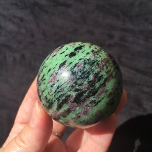 May include: A green, black and pink gemstone sphere. The sphere is smooth and polished.
