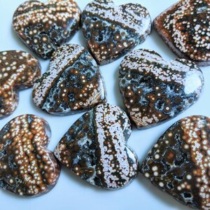 May include: A collection of eight heart-shaped ocean jasper stones. The stones are a mix of brown, white, and black with a speckled pattern.