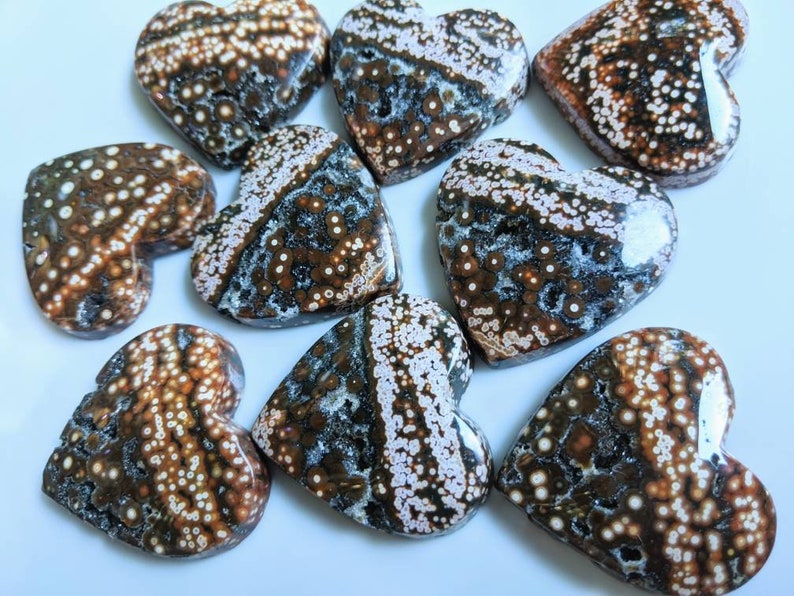 May include: A collection of eight heart-shaped ocean jasper stones. The stones are a mix of brown, white, and black with a speckled pattern.
