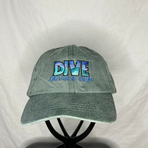 May include: A green baseball cap with the words "DIVE DEVIL'S DEN" embroidered in blue and white.