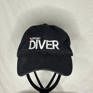 May include: Black baseball cap with a white embroidered logo that says "SPORT DIVER" with a red and white scuba diving flag.
