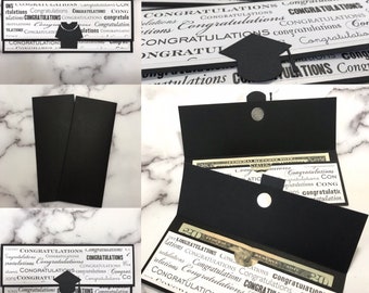 May include: Black card holder with a graduation cap design. The card holder is open to reveal a twenty dollar bill and a five dollar bill. The card holder is decorated with the word "Congratulations" repeated many times.