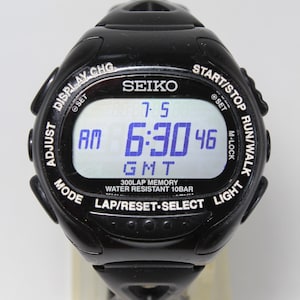 May include: Black Seiko digital watch with a display showing the time as 6:30 AM GMT. The watch has multiple buttons for adjusting settings and features a 300-lap memory and water resistance up to 10 bar.
