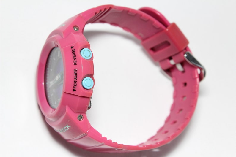 Puede incluir: Un reloj digital rosa con una esfera azul y dos botones azules que dicen "Forward" y "Reverse".