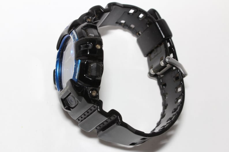 May include: Black digital watch with a blue accent around the face. The watch has a black band with a buckle closure. The watch is designed for sports and outdoor activities.
