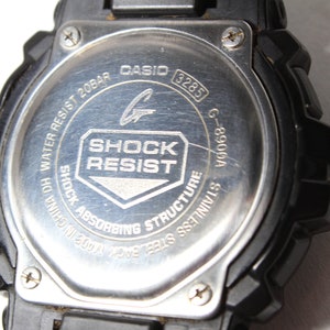 May include: Close-up of the back of a black Casio G-Shock watch. The stainless steel back features the text "SHOCK RESIST" and "WATER RESIST 20BAR". The model number G-8900A is also visible.
