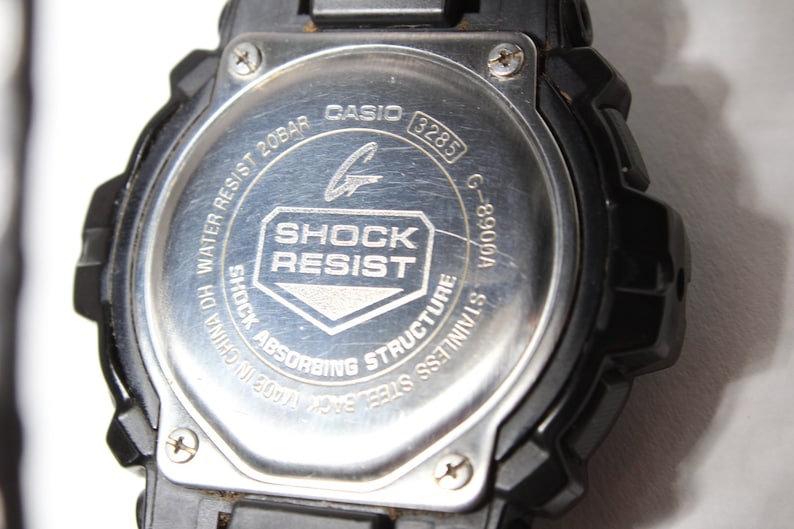 May include: Close-up of the back of a black Casio G-Shock watch. The stainless steel back features the text "SHOCK RESIST" and "WATER RESIST 20BAR". The model number G-8900A is also visible.