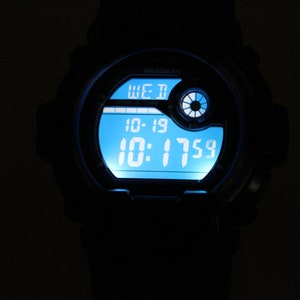 May include: A black digital wristwatch with a bright blue illuminated display. The watch face shows the day, date, and time: Wednesday, 10-19, and 10:17:59. The watch has a round face and a black band.
