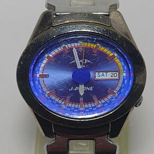 May include: A silver wristwatch with a blue face and a matching strap. The watch face shows "SAT 20" and the brand name "J-P ONE". The watch has a round face with a blue and red dial.