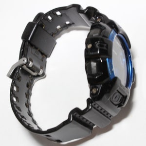 May include: Black digital watch with a blue bezel and a black strap. The watch has a silver buckle and a textured strap design. The watch is designed for sports and outdoor activities.
