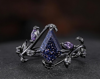 May include: Black ring with a dark blue, sparkly, square-shaped gemstone surrounded by delicate, black, leaf-shaped accents and smaller purple gemstones.