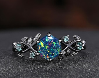 May include: Black ring with a large iridescent opal gemstone surrounded by smaller green gemstones and leaf-shaped accents.