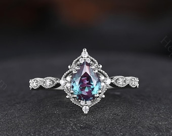 May include: A pear-shaped, iridescent gemstone ring set in a silver band with a delicate, vintage-inspired design. The ring features a halo of smaller diamonds surrounding the center stone.