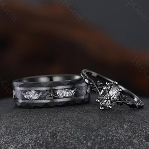 May include: A black wedding ring set. One ring has a hammered texture with silver leaf accents. The other ring has a black band with a central oval-shaped stone and black accent stones.