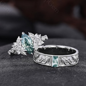 May include: Two silver rings with intricate floral and leaf designs. One ring features a large, pear-shaped green gemstone, while the other has a rectangular green stone set in a band with engraved details. The rings are displayed on a dark, textured surface.
