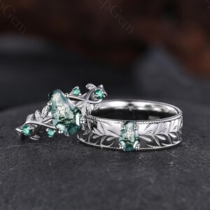 May include: Two silver rings with green gemstones. One ring features a floral design with a large, oval-shaped green stone and smaller accent stones. The other ring has a band with a leaf pattern and a central green stone.