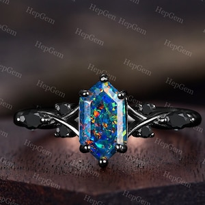 May include: A black ring with a large, octagon-shaped opal gemstone. The opal is a vibrant blue with flashes of green, red, and orange. The ring has a delicate, twisted band with small black gemstones.