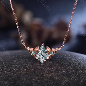 Könnte beinhalten: Eine zarte Halskette aus Roségold mit einem Anhänger aus grünem Moosachat, umgeben von kleinen grünen Edelsteinen und floralen Akzenten.