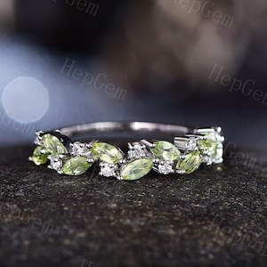May include: A delicate silver band ring featuring a row of marquise-shaped green peridot gemstones and small round diamonds.