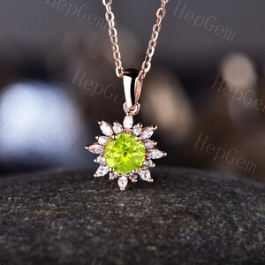 May include: A gold necklace with a green gemstone pendant surrounded by smaller white gemstones. The pendant is shaped like a flower.