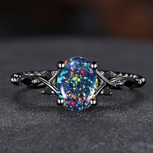 May include: A black ring with an oval-shaped opal gemstone. The opal displays a vibrant array of colors, including blue, green, and red. The ring's band features a detailed, ornate design.