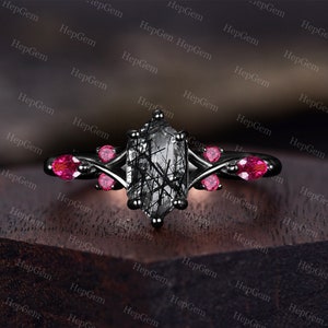 May include: Black engagement ring with a large, rectangular, clear gemstone with black inclusions. The ring has a black metal band with four small, red gemstones on each side of the center stone.